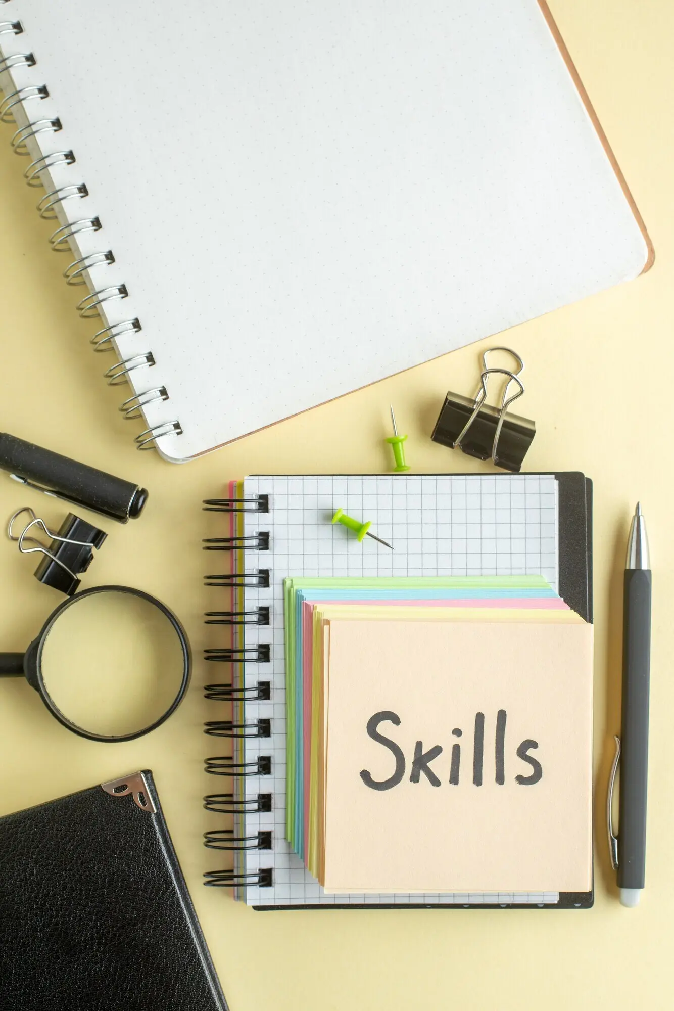 Draufsicht: Ein Zettel mit der Aufschrift „Fähigkeiten“ zusammen mit bunten kleinen Papierzetteln auf hellem Hintergrund; Notizblock, Job, Stift, Schule, Büro, Geschäft, Geld, Farbe, Arbeit, Heft.